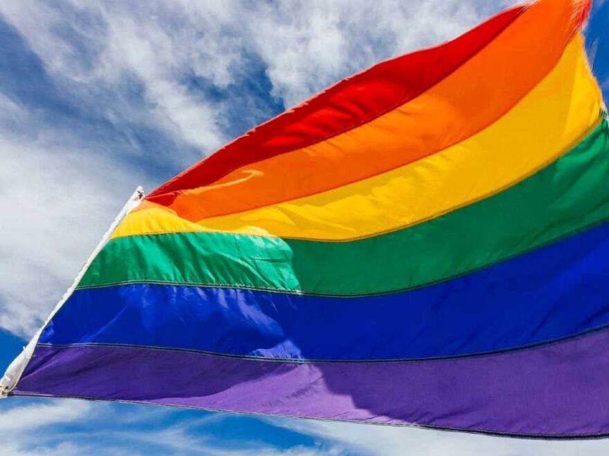 The Gay Pride flag flying against a blue sky